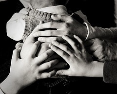 Baby with back to camera being held and hands of family placed on back