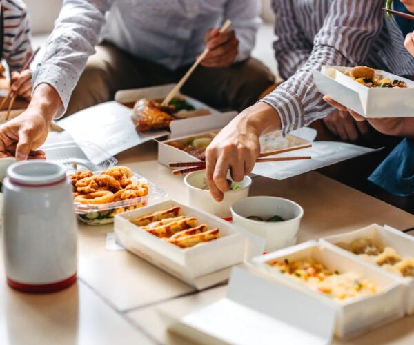 Group of people sitting at low table eating take out lunch from containers.