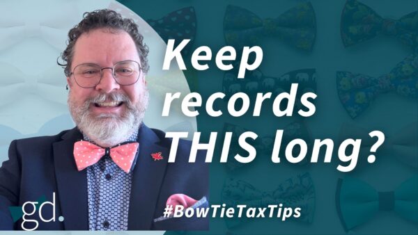 White male, dark curly hair, whitish beard, wearing glasses, a dark suit jacket, light shirt and purple bow tie talking about how long to keep tax records in Canada